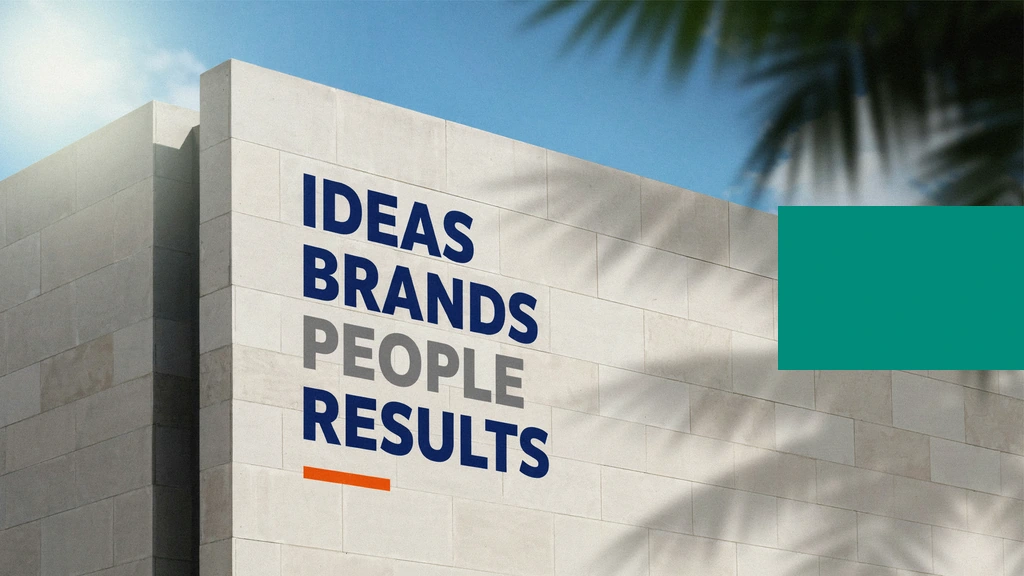 Un muro de hormigón con las palabras “Ideas Brands People Results”, cruzado por la sombra de unas palmas.